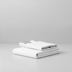 Összehajtott fehér szállodai asztalterítő és összehajtott fehér szállodai szalvéta benne kés és villa